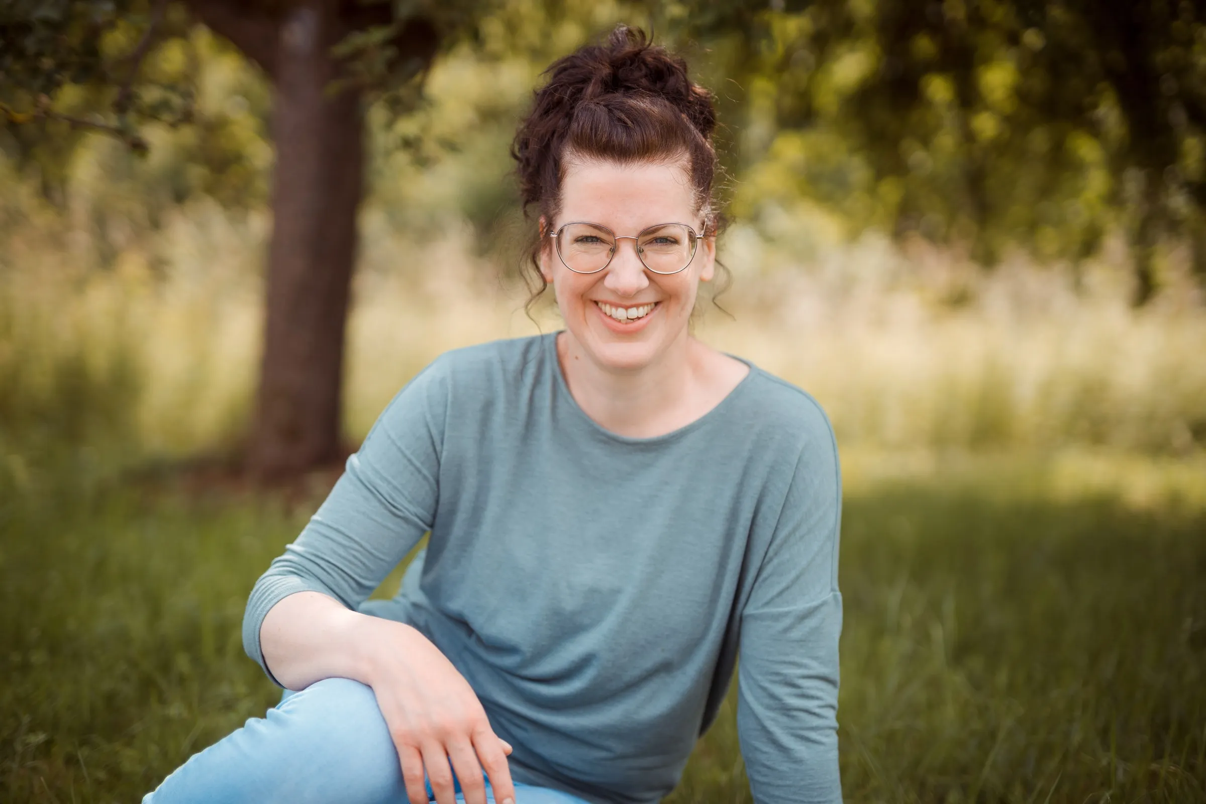 Carolin Reuter sitzt lächelnd im Gras unter einem Baum